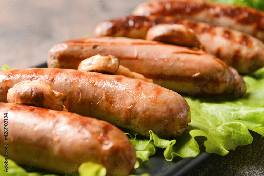 Plate with delicious grilled sausages on grunge background, closeup