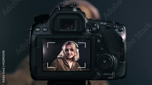 Young content creator blonde talking girl filming herself using a camera on a tripod while recording a vlog. Working from home