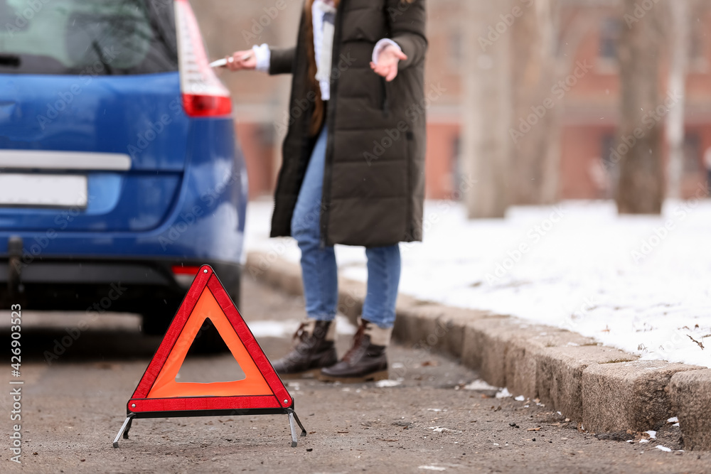 Emergency stop sign and stressed young woman near broken car outdoors