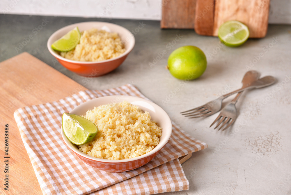 Bowls with tasty couscous and lime on table