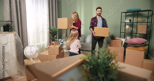 Happy Caucasian family couple moving home into new apartment with adorable little girl daughter discussing redecoration of furniture unpacking boxes and getting settled. Home comfort. Relocating day photo