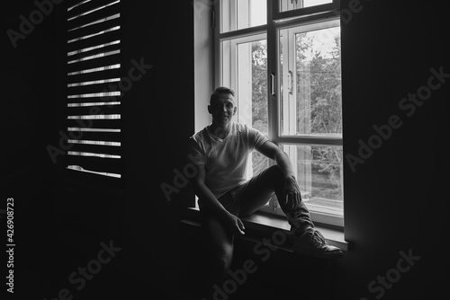 A man in a T-shirt sits by the window