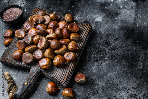 Raw chestnuts on a wooden cutting board. Black background. Top view. Copy space
