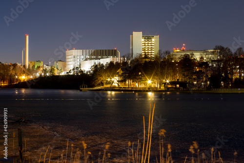 Nightly view of Meilahti district in Helsinki with illuminated white buildings casting reflections on the water surface.
