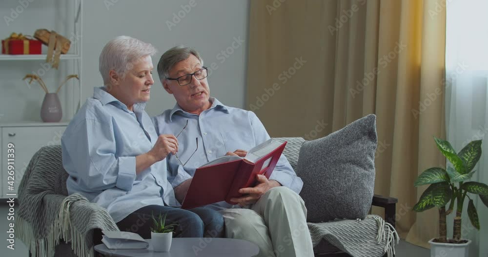 Two old people elderly couple missed husband and wife sitting on sofa in cozy living room remember pleasant moments from past looking at pictures of their beloved children,turn pages of photo album Two old people elderly couple missed husband and wife sitting on sofa in cozy living room remember pleasant moments from past looking at pictures of their beloved children,turn pages of photo album