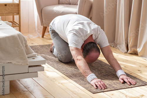 Active senior man doing the child pose while practicing yoga on a mat