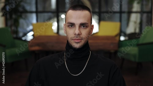 Portrait of young stylish caucasian guy raising head and looking to camera. Portrait of handsome man with bristles and chainlet posing. Blurred background. photo