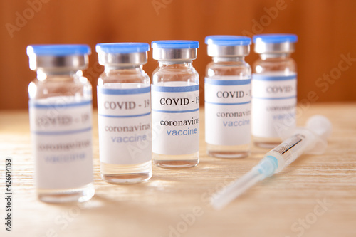 Vaccine ampoules and syringe, coronavirus medical concept on brown background