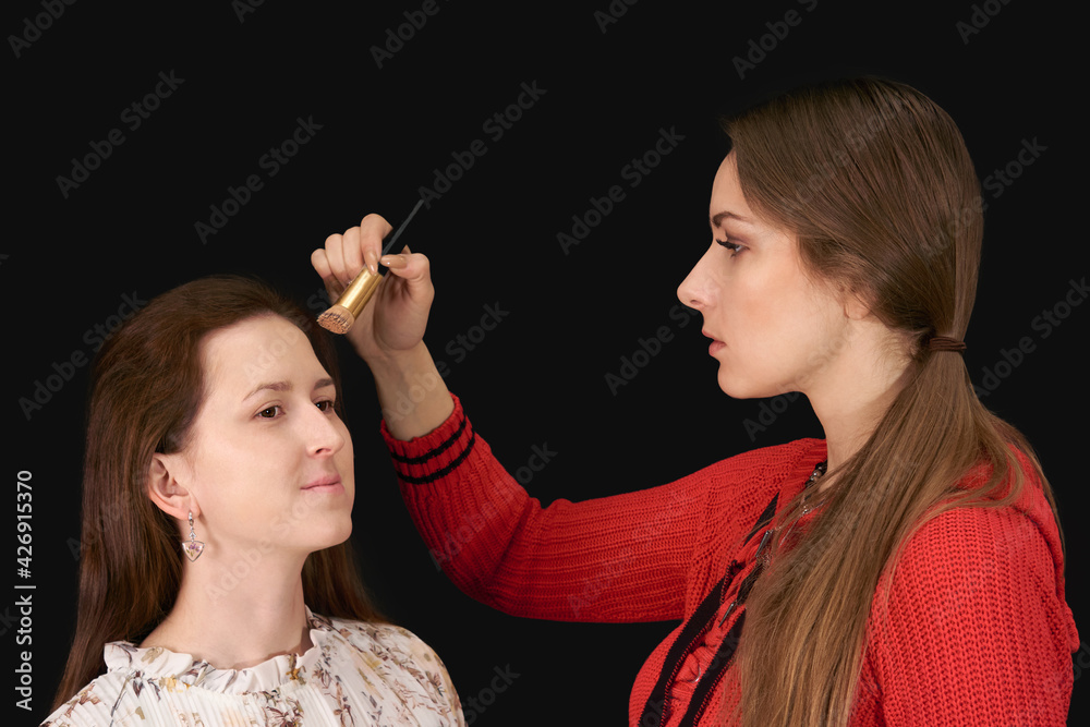 female makeup artist applies cosmetics to model on dark background female makeup artist applies cosmetics to model on dark background