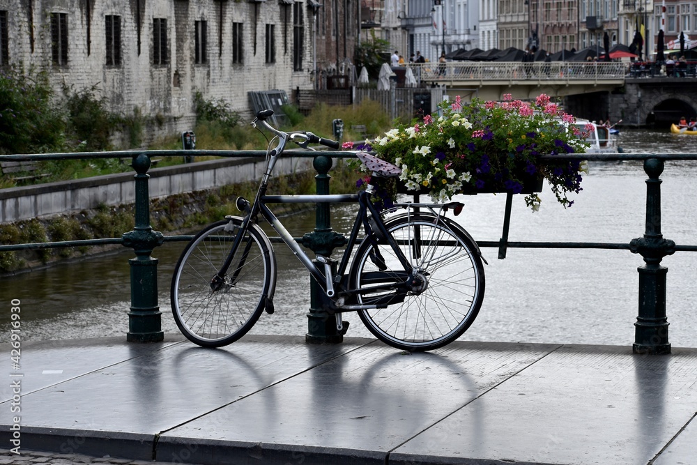 Bicycle parked over a canal next to flowers in Ghent