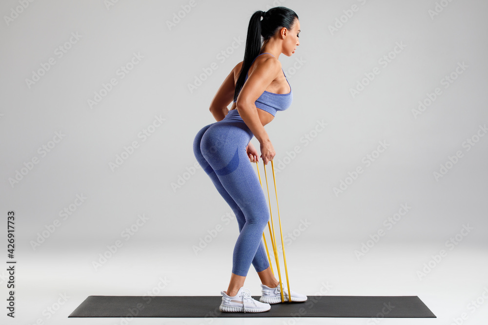 Fitness woman doing exercise with resistance band on gray background. Athletic girl working out