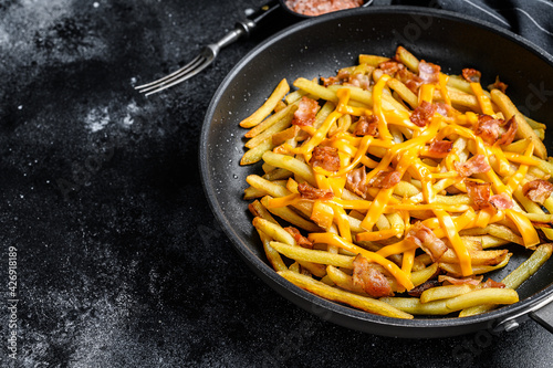 French fries baked with cheddar cheese and bacon in a pan. Black background. Top view. Copy space