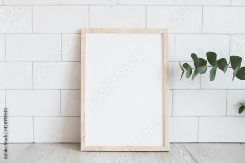 Blank wooden vertical picture frame mockup and eucalyptus on table. Modern home interior, Scandinavian style. White tiles wall background. © photoguns