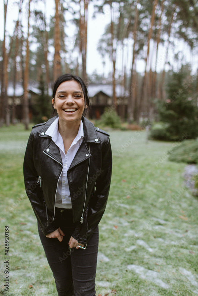 Beautiful brunette in a leather jacket laughs while walking in the woods Beautiful brunette in a leather jacket laughs while walking in the woods