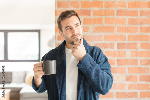 Obraz na plátně handsome man smiling with a happy, confident expression with hand on chin, wonde
