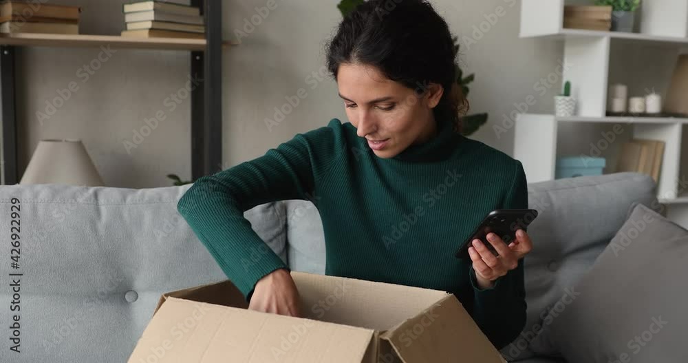 Happy millennial beautiful woman typing positive feedback or sharing good customer shopping experience on internet store website using cellphone, feeling satisfied with received purchase at home.