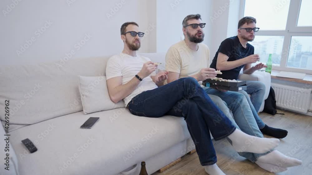 Group of friends are watching movie on TV while eating pizza and drinking beer sitting in the living room at home. They are wearing 3D glasses and discussing the film Group of friends are watching movie on TV while eating pizza and drinking beer sitting in the living room at home. They are wearing 3D glasses and discussing the film