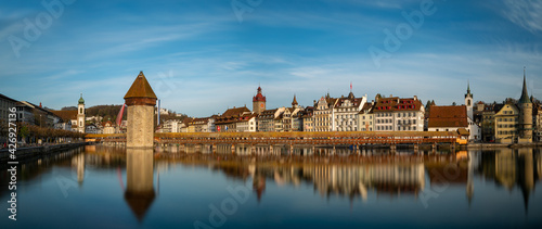 Panoramic view of the Chapel bridge in Lucern, Switzerland. Long exposure with bridge and city skyline reflecting on water against blue sky.
