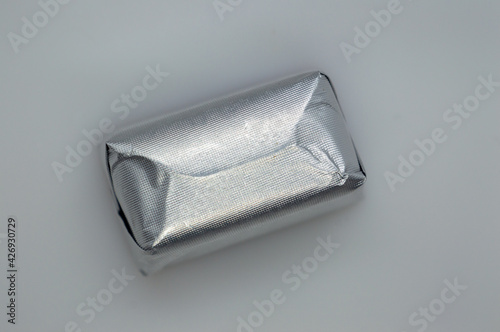 Chocolate candy wrapper in silver color. The shape is in the form of a square on a gray background. Isolated. Copy the space.