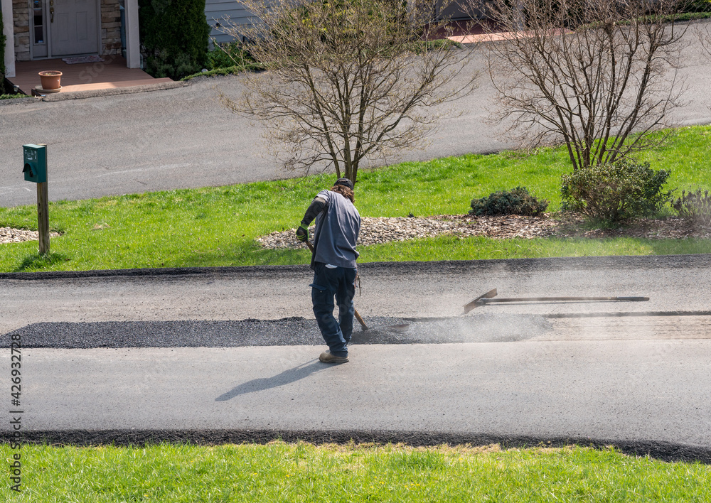 Worker applying a layer of tarmac or extra blacktop to repair damage to