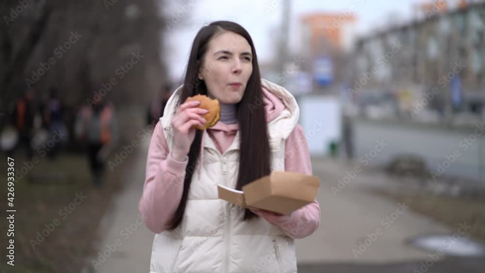 Pretty woman walking outdoors in the city and eating burger Pretty woman walking outdoors in the city and eating burger