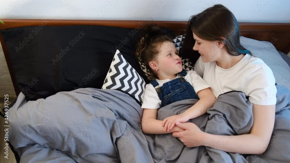 Top view of caring single mother talk little daughter lying on comfy bed at home. Affectionate worried young mom hug and supports cute child girl giving love protection. Psychological support concept Top view of caring single mother talk little daughter lying on comfy bed at home. Affectionate worried young mom hug and supports cute child girl giving love protection. Psychological support concept