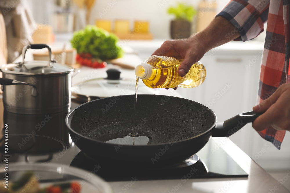 Man pouring cooking oil into frying pan in kitchen, closeup Stock Photo |  Adobe Stock