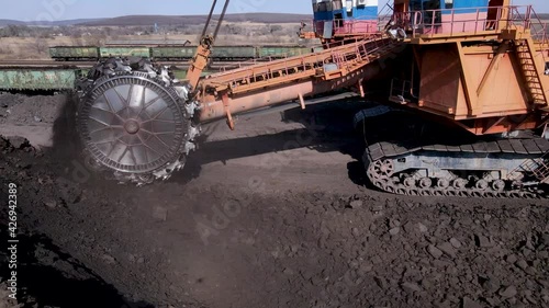 2021, Novoshakhtinsky, Russia - Extraction of coal. View from above. A large rotary excavator shovels coal from a coal heap with a bucket. Loading coal into railway wagons.