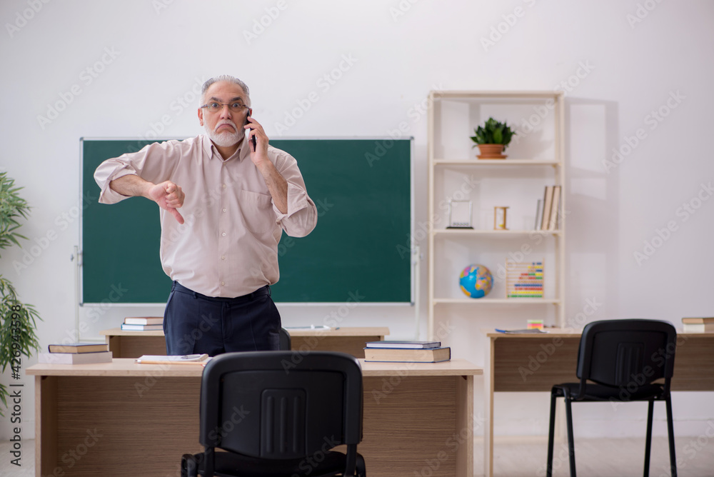 Old male teacher in front of blackboard