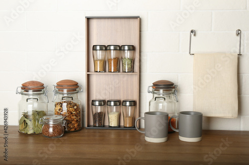 Set of spices and different dishware on wooden table near white brick wall in kitchen