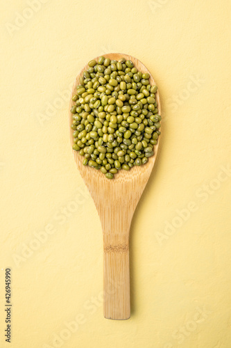 Portion of Asian beans in a wooden spoon on a yellow table. Concept of proper balanced nutrition and healthy food