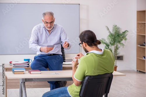 Old male teacher and young male student playing card in the clas