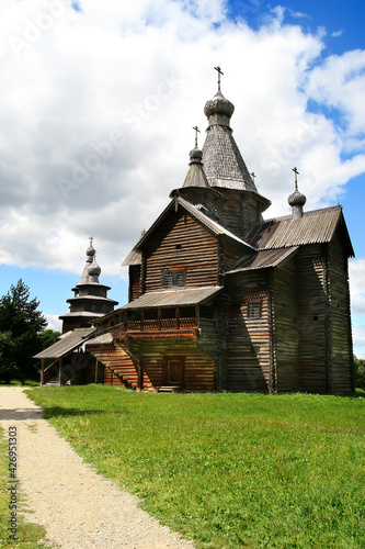 An old wooden church. A dirt path leads to the church. Against the background of a blue sky with cumulus clouds. 