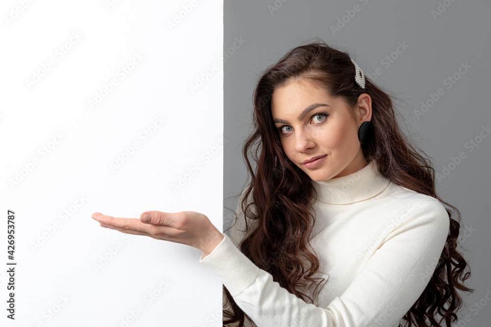 beautiful sensual woman with long curly hair shows a blank banner, isolated on gray, copy space beautiful sensual woman with long curly hair shows a blank banner, isolated on gray, copy space