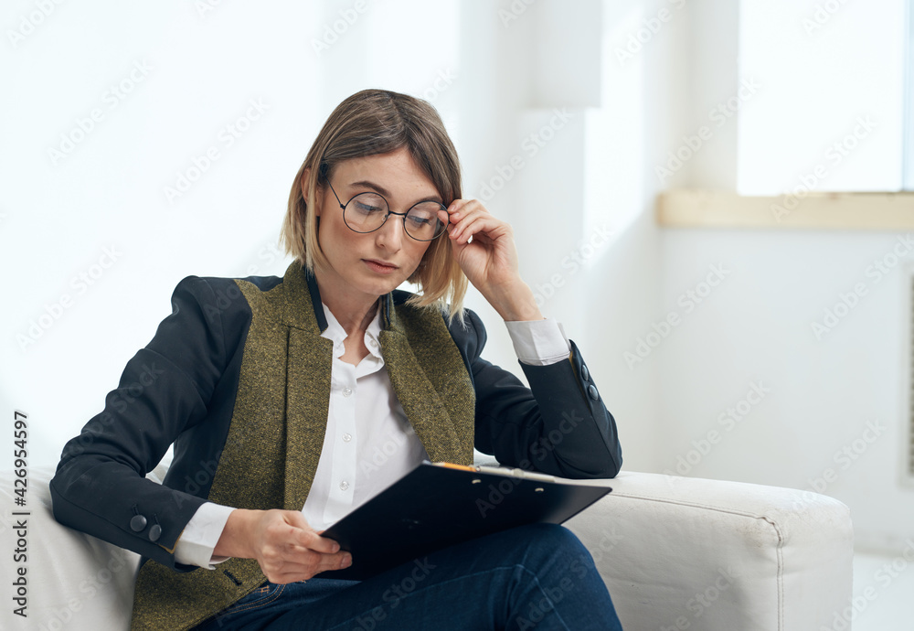 A woman in a jacket and trousers with a white sheet of paper in a folder near the window