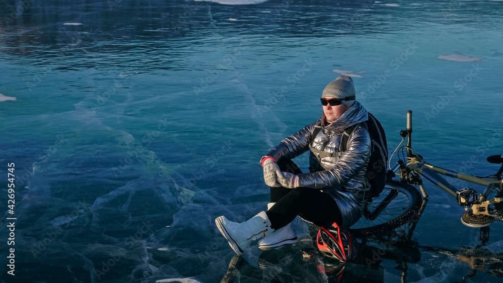 Woman sitting near her bike on ice. The girl cyclist stopped to Woman sitting near her bike on ice. The girl cyclist stopped to