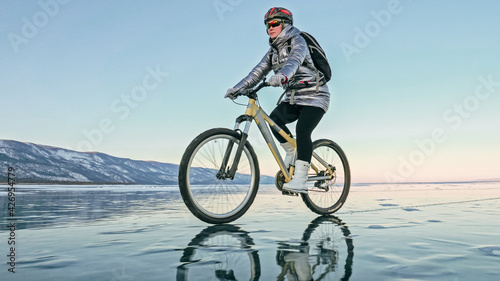 Fototapeta Naklejka Na Ścianę i Meble -  Woman is riding bicycle on the ice. Tires on bike are covered wi