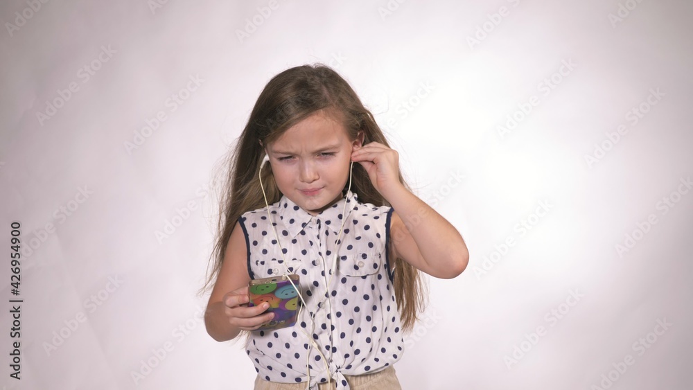 Child with headphones dancing at studio background. Girl listens to music on smartphone. Beautiful cute happy little girl listens to music. Child with headphones dancing at studio background. Girl listens to music on smartphone. Beautiful cute happy little girl listens to music.