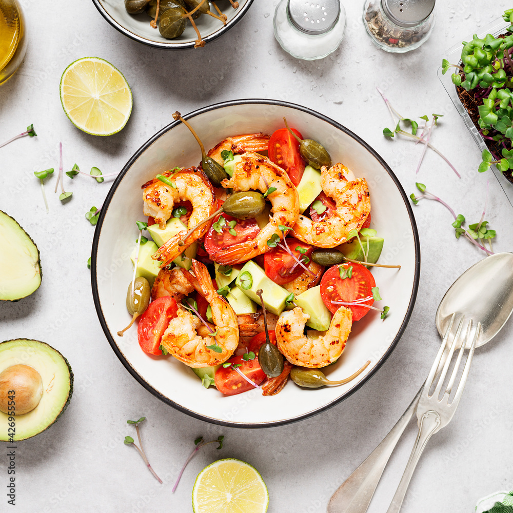 Easy grilled shrimp avocado salad with cherry tomatoes, capers and microgreens. Gray background. Top view. Easy grilled shrimp avocado salad with cherry tomatoes, capers and microgreens. Gray background. Top view.