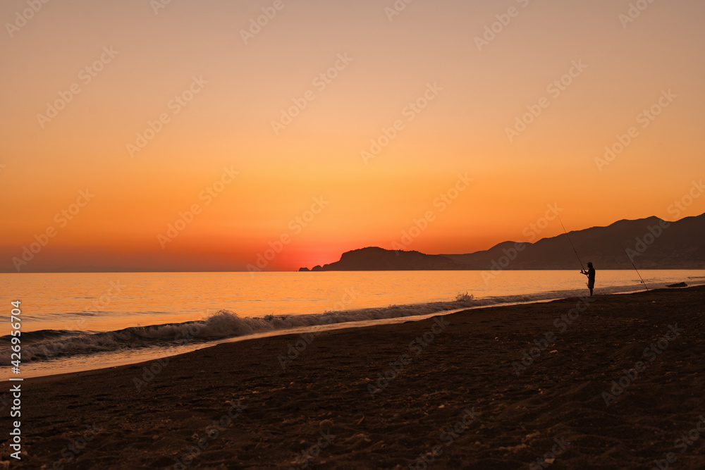 Fishing in the Sunrise on a sandy beach with a mountain on horizon