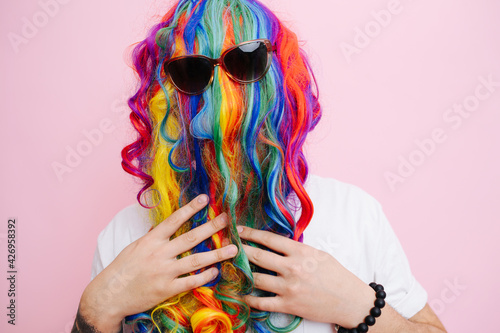 Extremely funny looking man in a wig over face and sunglasses over pink