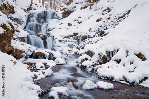 Small mountain waterfall of icy water flow among wet stones covered with white snow © YouraPechkin