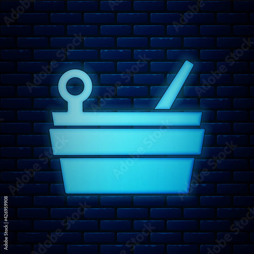 Glowing neon Sauna bucket and ladle icon isolated on brick wall background. Vector