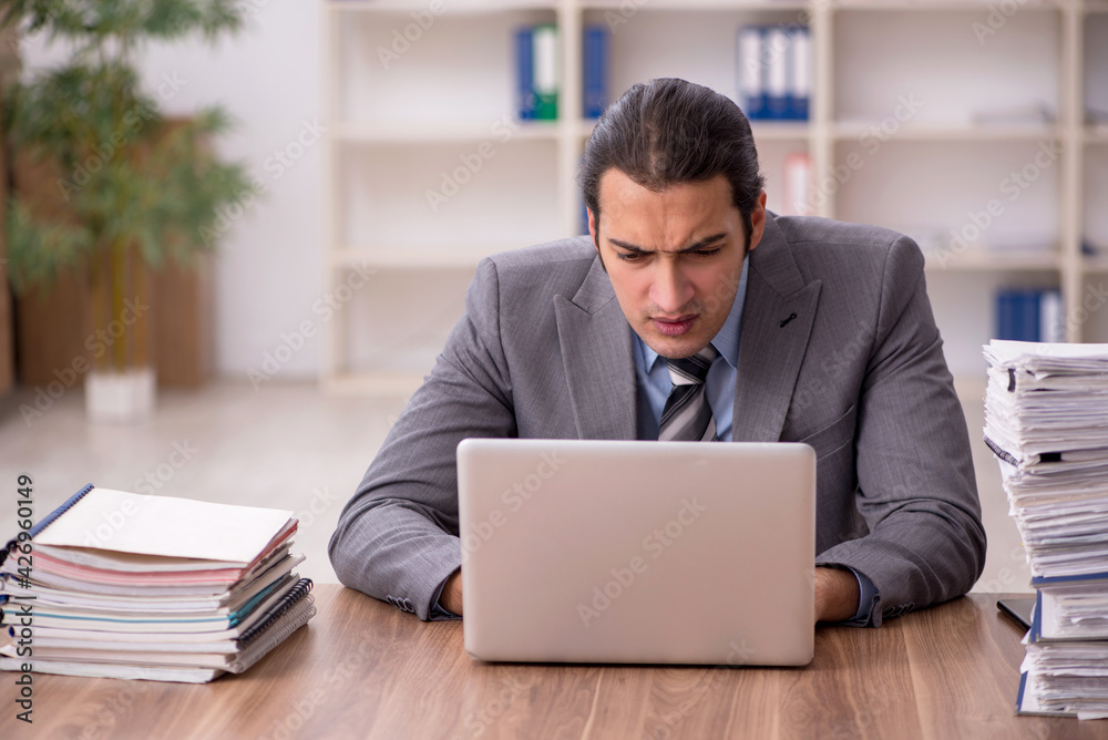 Young male employee unhappy with excessive work in the office Young male employee unhappy with excessive work in the office