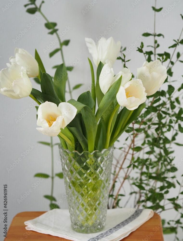 Glass vase with a bouquet of delicate white tulips with a yellow center on a gray background. Congratulatory background with place for text.