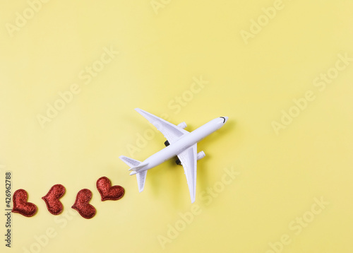 flat lay of airplane model with red hearts on yellow background. Honeymoon trip or travel lover concept.