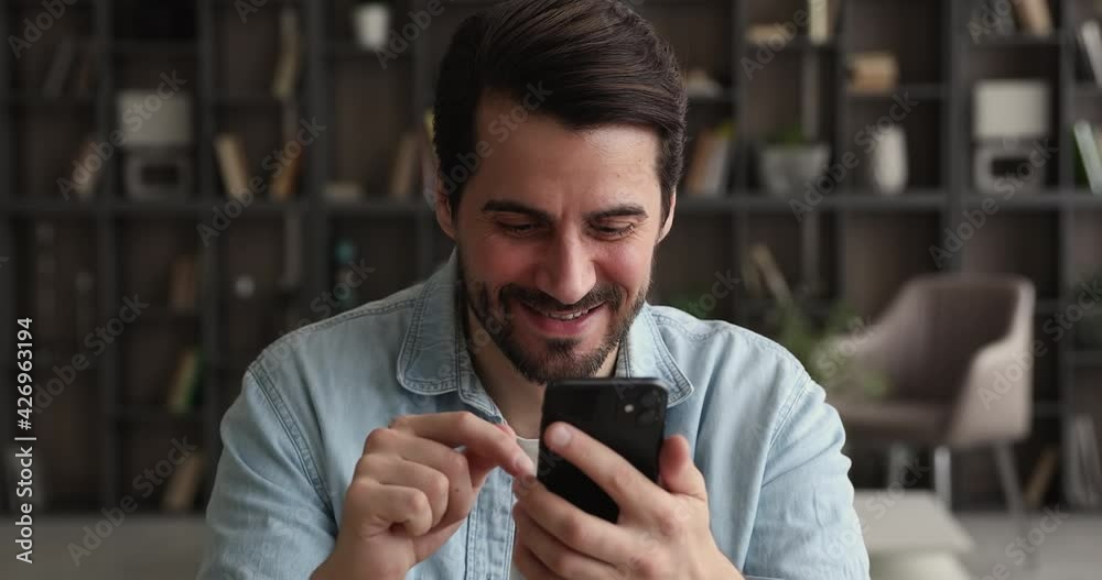Head shot addicted to modern technology smiling young caucasian man involved in communicating in social network or dating online, using software applications, playing mobile games on smartphone.