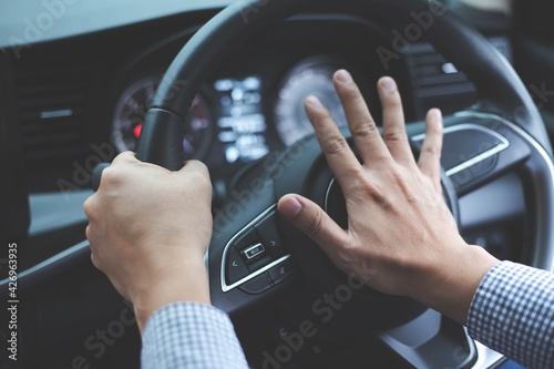 Close up image of inside the car of the hand pressing the horn on the steering wheel.Safe driving concept photo