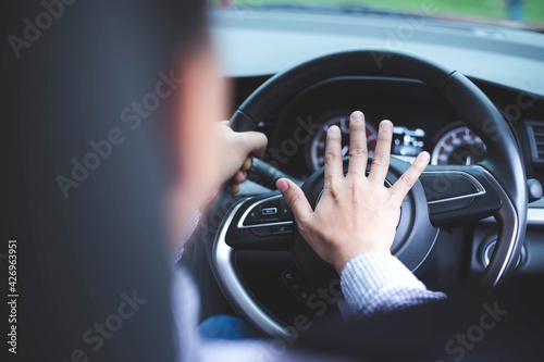 Close up image of inside the car of the hand pressing the horn on the steering wheel.Safe driving concept photo