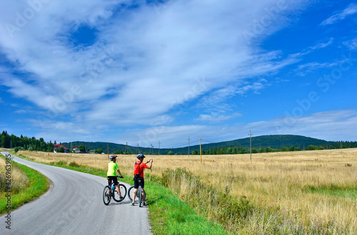 Back view of male cyclist holding cell phone and taking picture of beautiful hills. They get a lot of fun riding together.